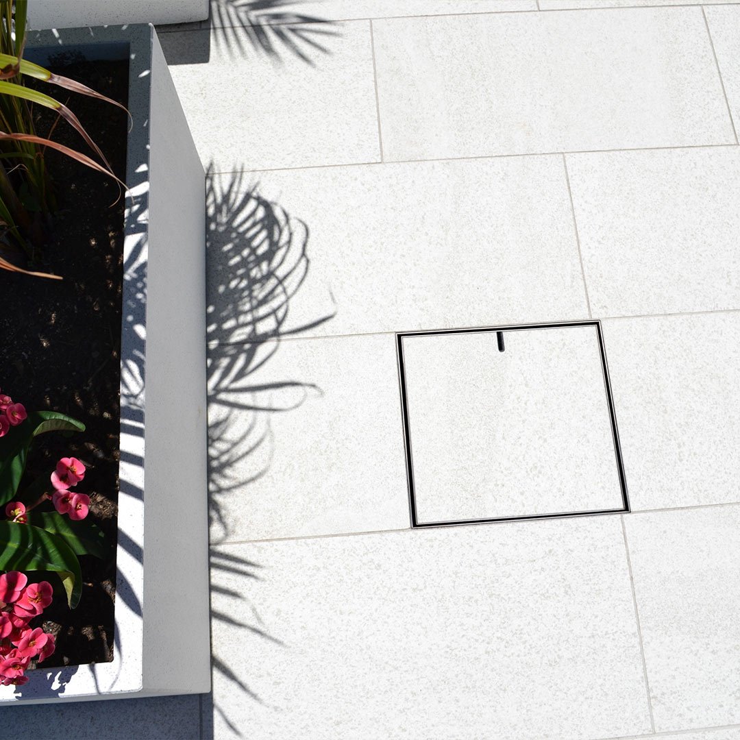 HIDE Drain Cover with white paving stone inlay installed into french pattern pavers