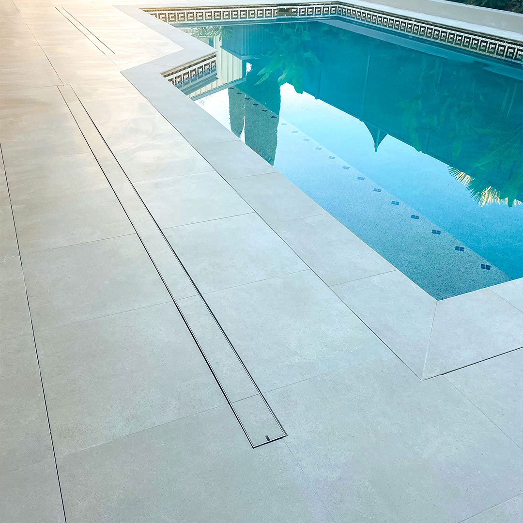 HIDE stainless steel Linear Strip Drain Cover with grey tile inlay installed next to swimming pool.