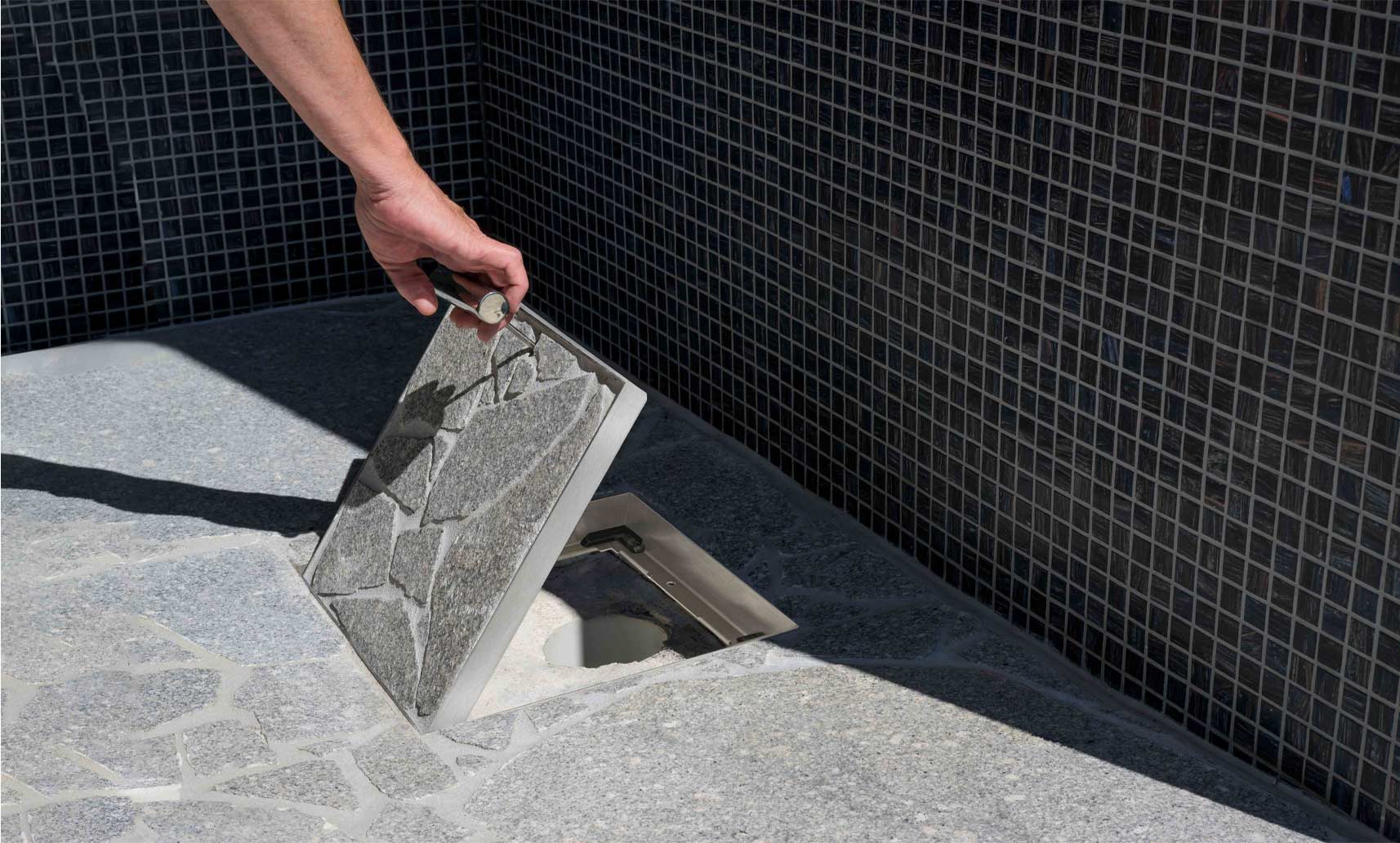 HIDE Drain Cover with grey crazy pave being opened to view drainage pipe underneath.